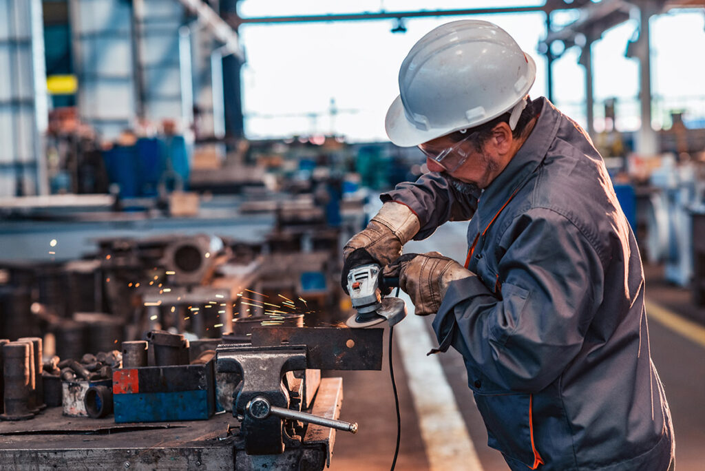 An industrial worker grinding a metal machine part.