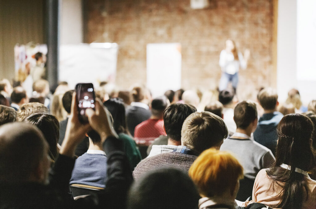 An auditorium of people listening to a speaker on stage.