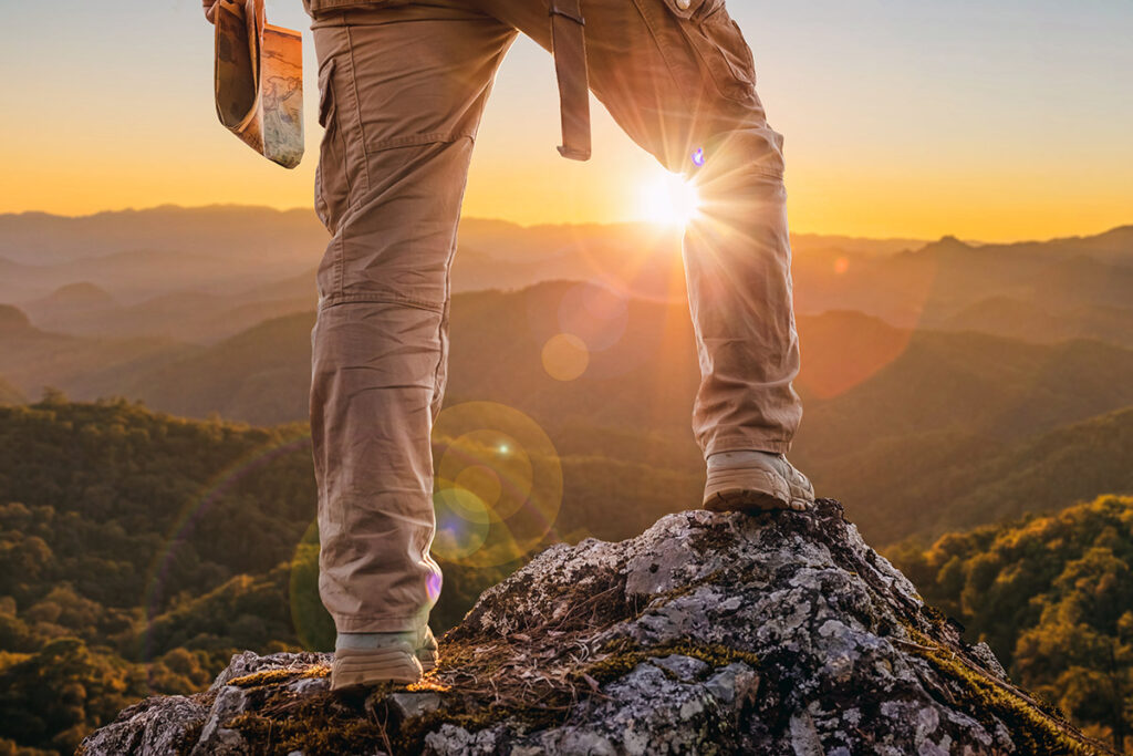 Man standing atop mountain peak overlooking scenery.