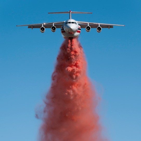 An Aero-Flite fire bomber plane flying directly at the camera dropping a load of red fire retardant.
