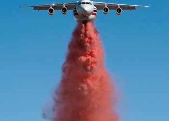 An Aero-Flite fire bomber plane flying directly at the camera dropping a load of red fire retardant.